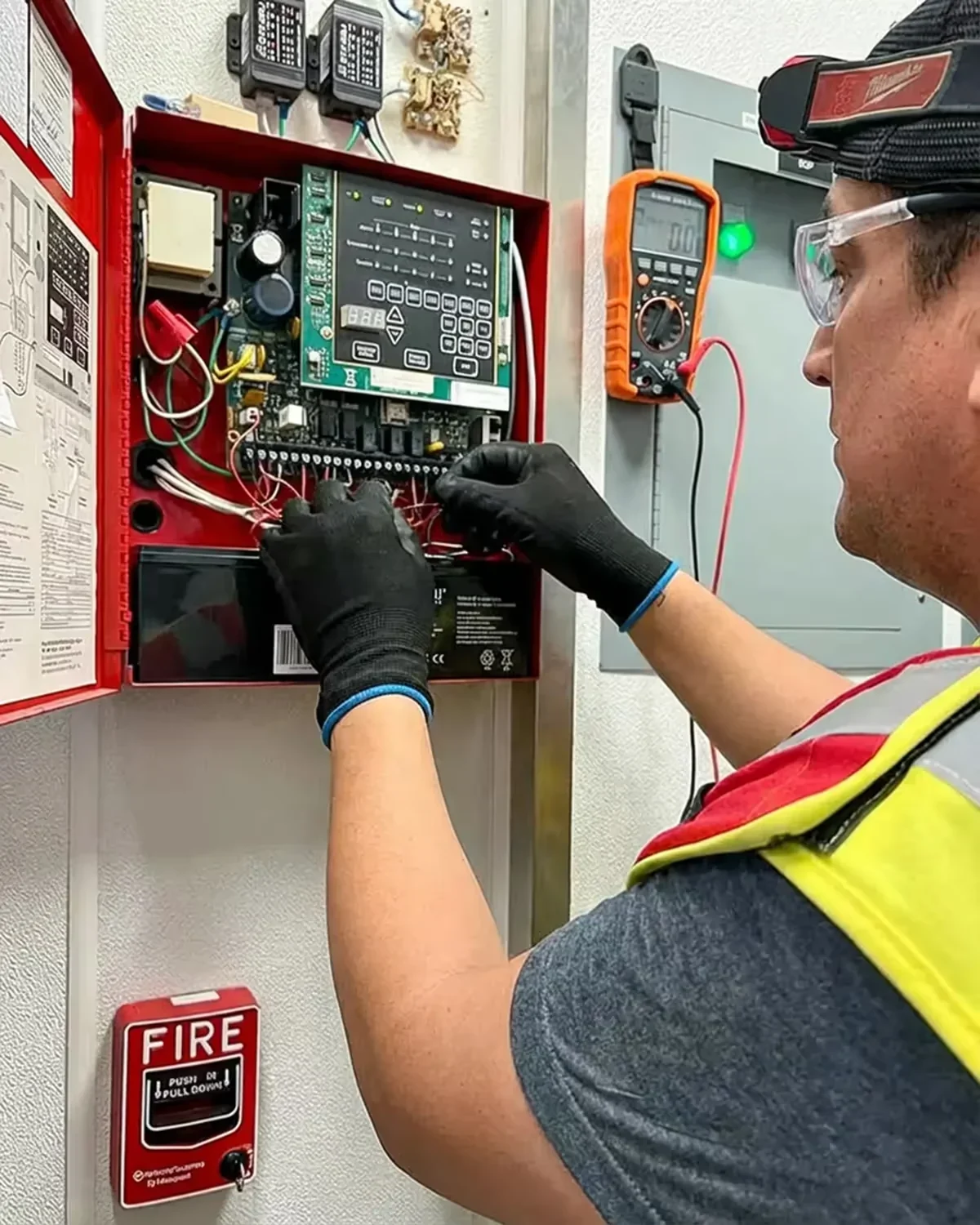 Technician testing an open fire alarm control panel with a multimeter